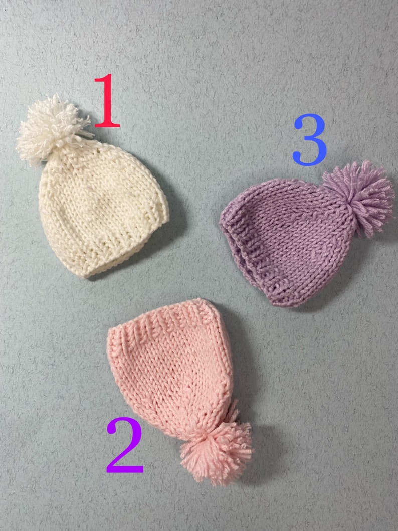 May include: Three knitted hats with pom-poms in white, pink, and purple. The hats are numbered 1, 2, and 3.
