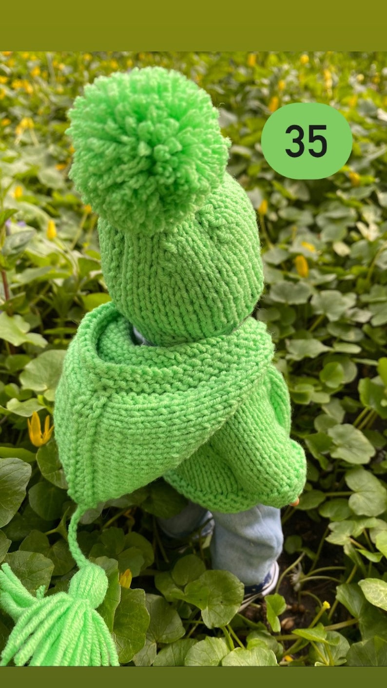 May include: A bright green knitted hat with a pom-pom on top and a matching green knitted scarf. The hat and scarf have a tassel detail. The number 35 is written on a green circle in the background.