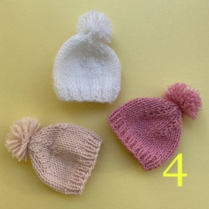 May include: Three knitted hats with pom-poms in white, pink, and light pink.