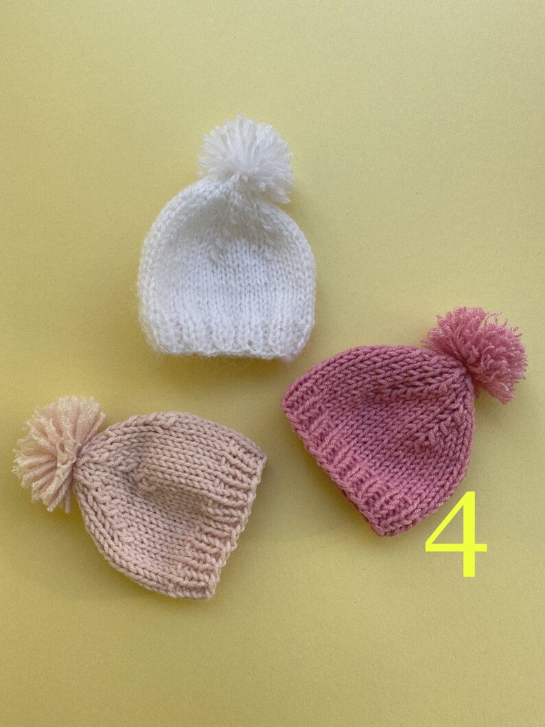 May include: Three knitted hats with pom-poms in white, pink, and light pink.