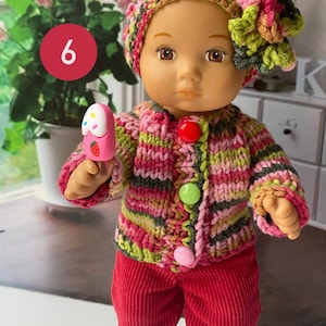 Puede incluir: Una mu&ntilde;eca con un c&aacute;rdigan de punto a rayas rosa, verde y marr&oacute;n con un gorro a juego y una flor rosa. La mu&ntilde;eca sostiene un helado de juguete rosa y blanco. La mu&ntilde;eca lleva pantalones de pana roja y zapatillas blancas con detalles rosas.