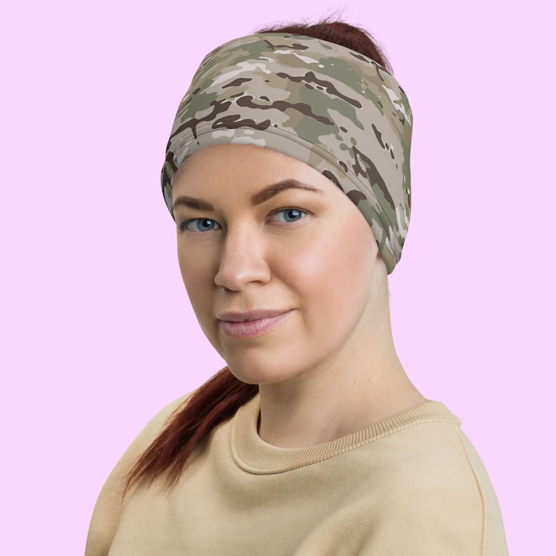 May include: A woman wearing a camouflage headband. The headband is made of a soft, stretchy fabric and has a  camouflage pattern in shades of green, brown, and tan.