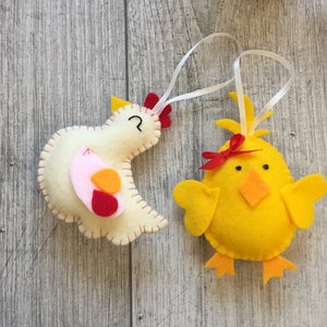 Peut inclure: Deux décorations de poulet en feutre, une jaune et une blanche avec des accents rouges, roses et orange. Les décorations ont des boucles de ficelle blanches pour accrocher.