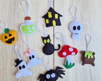 May include: A collection of Halloween-themed felt ornaments. Includes a jack-o'-lantern, potion bottle, haunted house, skull, black cat, mushroom, cauldron, spider, and ghosts. Each ornament has a white ribbon for hanging.