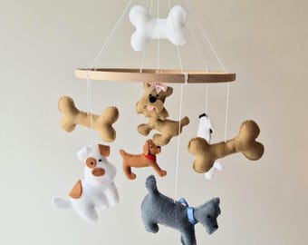Könnte beinhalten: Ein Babymobile mit Filzhundefiguren und Knochenformen in verschiedenen Farben, darunter Weiß, Braun und Grau. Das Mobile ist an einem Holzreifen mit weißer Schnur aufgehängt.