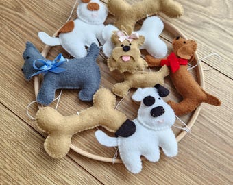 Könnte beinhalten: Eine Sammlung handgefertigter Hundeornamente aus Filz in verschiedenen Farben, darunter Weiß, Grau und Braun. Jeder Hund hat einzigartige Merkmale wie Flecken, Schleifen und rote Schals. Die Ornamente sind auf einem Holzreifen angeordnet.