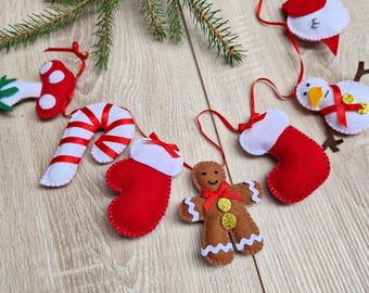 Könnte beinhalten: Eine Weihnachtsgirlande aus Filz mit roten und weißen Zuckerstangen, einem Lebkuchenmann, einem Strumpf, einem Pilz, einem Schneemann und einem Vogel. Die Girlande ist auf einem weißen Band aufgefädelt.