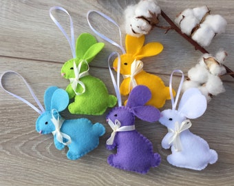 May include: Five felt bunny ornaments in different colors: green, yellow, blue, purple, and white. Each bunny has a white ribbon tied around its neck.