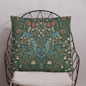 May include: A green throw pillow with a floral pattern featuring red, blue, and yellow flowers. The pillow is sitting on a metal chair with a white cushion.