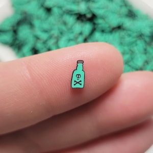 May include: A small, teal green glass bottle with a cork top and the text "6x" printed on the front. The bottle is being held by a finger.