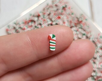May include: A close-up of a small, red and white candy cane with green stripes. The candy cane is being held by a finger.