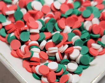 May include: A white plate filled with red, white, and green round sprinkles. The sprinkles are perfect for decorating cakes, cupcakes, and other desserts.