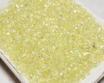 May include: A white square dish filled with yellow glass glitter. The glitter is small and has a slight iridescent sheen.