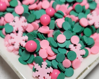 May include: A white plate filled with pink and green sprinkles. The sprinkles are in the shape of circles and snowflakes.