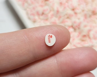 May include: A close-up of a white round sticker with a red candy cane design. The sticker is being held by a finger.