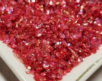May include: A white ceramic dish filled with iridescent red glitter. The glitter is small and has a variety of shapes.
