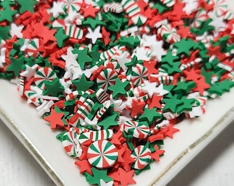 May include: A white ceramic plate filled with red, green, and white Christmas sprinkles. The sprinkles are shaped like stars, candy canes, and peppermint swirls.