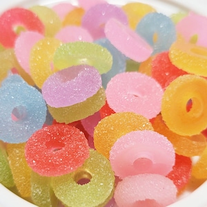 May include: A white bowl filled with colorful, donut-shaped candies. The candies are in shades of pink, yellow, orange, blue, and purple.