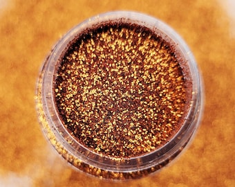 May include: A small clear jar filled with copper glitter. The glitter is scattered around the jar on a white surface.