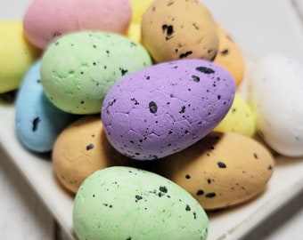 May include: A white plate filled with colorful speckled Easter eggs in shades of pink, yellow, green, purple, and white.