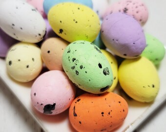 May include: A white plate with a pile of colorful speckled Easter eggs in various shades of pink, blue, green, yellow, and purple.