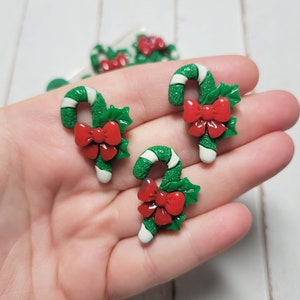 May include: Three green and white candy cane ornaments with red bows and holly leaves.