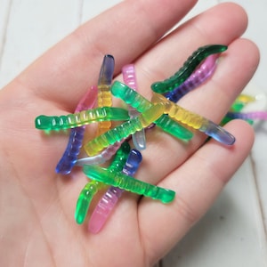 May include: A collection of colorful, translucent, plastic worm-shaped toys. The worms are in various shades of green, blue, yellow, and pink.