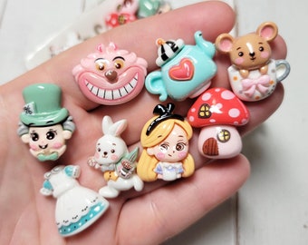 May include: A set of nine Alice in Wonderland themed resin cabochons. The cabochons feature characters like the Mad Hatter, Alice, the Cheshire Cat, and the White Rabbit. The cabochons are perfect for crafting projects like jewelry, hair clips, and keychains.