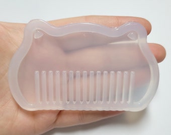 May include: A clear silicone mold shaped like a cat's head with a comb design on the bottom. The mold is designed for making resin crafts.