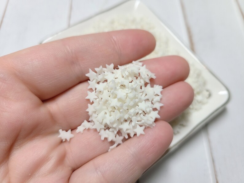 May include: A small white bowl filled with white star-shaped sprinkles. The sprinkles are small and delicate, perfect for decorating cakes, cupcakes, or cookies.