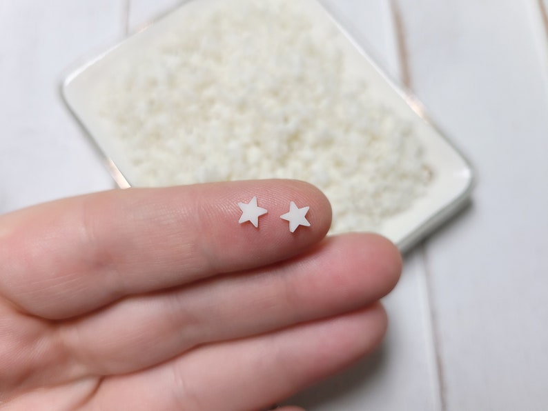 May include: Two small white star-shaped embellishments on a finger.