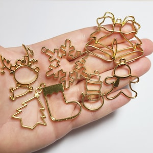 May include: A set of eight gold-colored metal Christmas ornament blanks. The ornaments include a snowflake, a stocking, a Christmas tree, a reindeer, a snowman, a bell, and two gingerbread people.