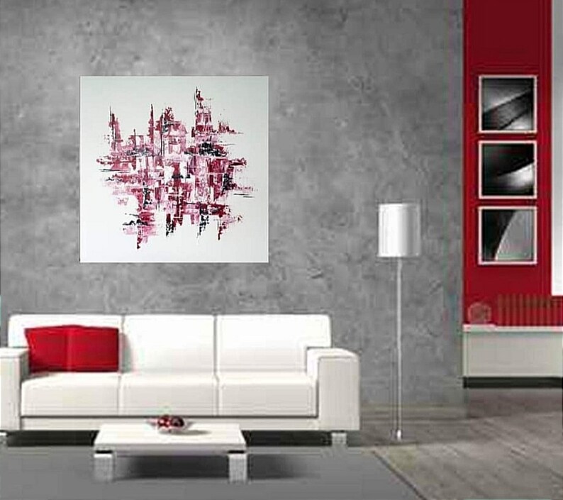 May include: Abstract painting on a white canvas. The artwork features a cityscape design in shades of red and black. The painting is displayed on a gray wall above a white sofa with a red pillow. A modern interior design.