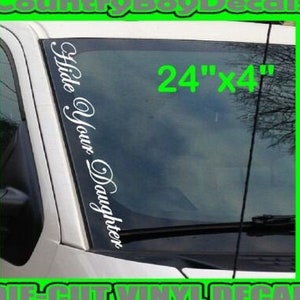 May include: White vinyl decal with the text "Hide Your Daughter" in a cursive font. The decal is 24 inches long and 4 inches wide. It is shown on a car windshield.