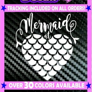 Könnte beinhalten: Weißer Vinyl-Aufkleber mit dem Text "Mermaid at Heart" und einem herzförmigen Design aus Meerjungfrauen-Schuppen. Der Aufkleber befindet sich auf einem schwarz-weißen Carbonfaser-Hintergrund. Über 30 Farben sind verfügbar.