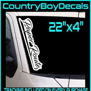 May include: White vinyl decal with the text "Paper Route" in a cursive font. The decal is 22 inches by 4 inches. The decal is shown on a car windshield. The text "TRACKING INCLUDED ON EVERY PURCHASE" and "30+ Colors Available" are also shown in the image.