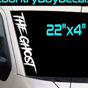 May include: White vinyl decal with the words "THE GHOST" in a stylized font. The decal is 22 inches by 4 inches and is shown on a car windshield. The text "30+ Colors Available" is also included.