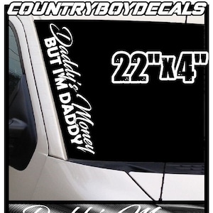May include: White vinyl decal with the text "Daddy's Money But I'm Daddy" in a cursive font. The decal is 22 inches by 4 inches. The decal is shown on a black truck windshield.