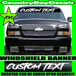 May include: A black truck with a white windshield banner that says "CUSTOM TEXT". The banner is 42 inches wide and 4.5 inches tall. The truck is in front of a green background.