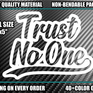 Può includere:  Adesivo in vinile bianco con il testo "Trust No One" in un font stilizzato. L'adesivo misura 7 pollici per 5 pollici ed è mostrato su uno sfondo nero in fibra di carbonio.
