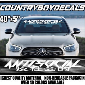 Puede incluir: Calcomanía de vinilo blanco con el texto "ANTISOCIAL" en una fuente estilizada con caracteres japoneses debajo. La calcomanía se muestra en el parabrisas de un coche plateado. La calcomanía mide 101,6 cm por 12,7 cm.