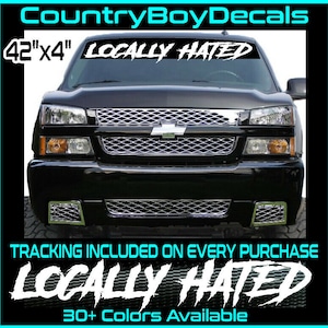 May include: A black truck with a chrome grill and headlights. A white decal that reads "LOCALLY HATED" is across the top of the windshield. The decal measures 42" x 4".