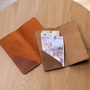 May include: Two brown leather wallets with a brown suede interior. One wallet has a few bills of Romanian Leu currency inside.