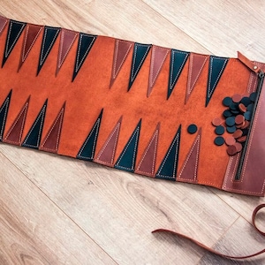Könnte beinhalten: Ein Backgammon-Set aus braunem Leder mit schwarzen und braunen Spielsteinen. Das Set ist zusammengerollt und hat einen Reißverschluss.