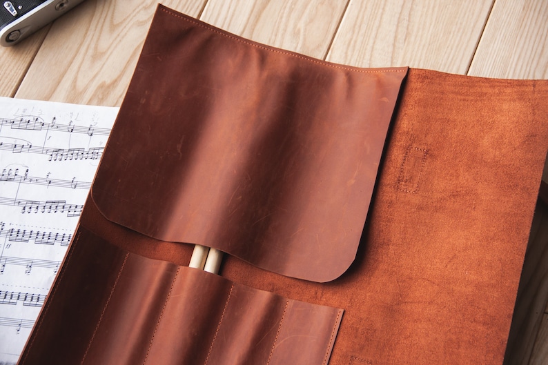 May include: A brown leather roll with multiple slots for holding drumsticks. The roll is open and two drumsticks are visible inside.