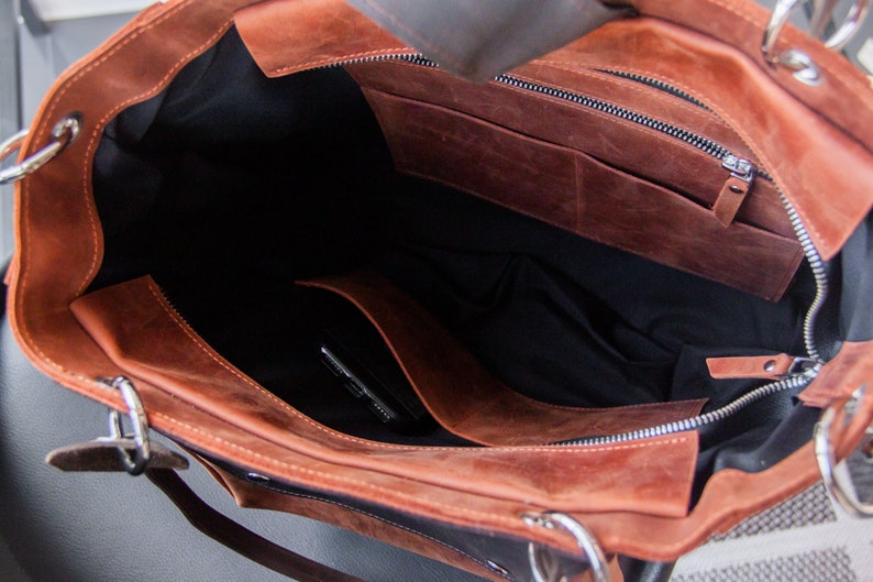 K&ouml;nnte beinhalten: Das Innere einer braunen Ledertasche mit schwarzem Stofffutter. Die Tasche hat eine Rei&szlig;verschlusstasche und eine kleinere offene Tasche im Inneren.