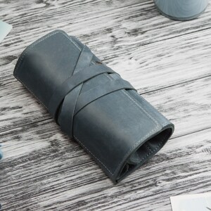 May include: A blue leather pencil case with a rolled design and a strap closure.