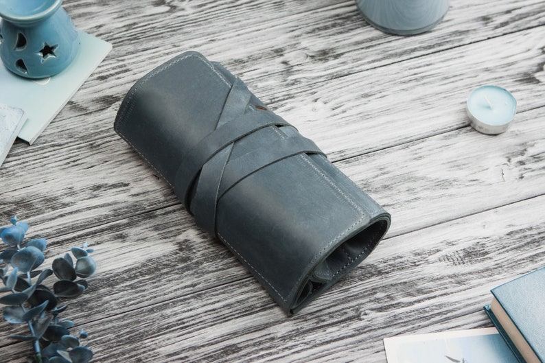 May include: A blue leather pencil case with a rolled design and a strap closure.