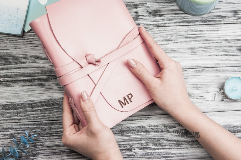 May include: A pink leather journal with a leather tie closure and the initials "MP" embossed on the front.
