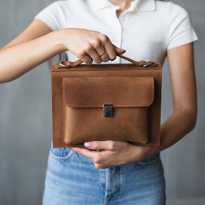 May include: A brown leather briefcase with a silver clasp. The briefcase has a flap that closes with a buckle.